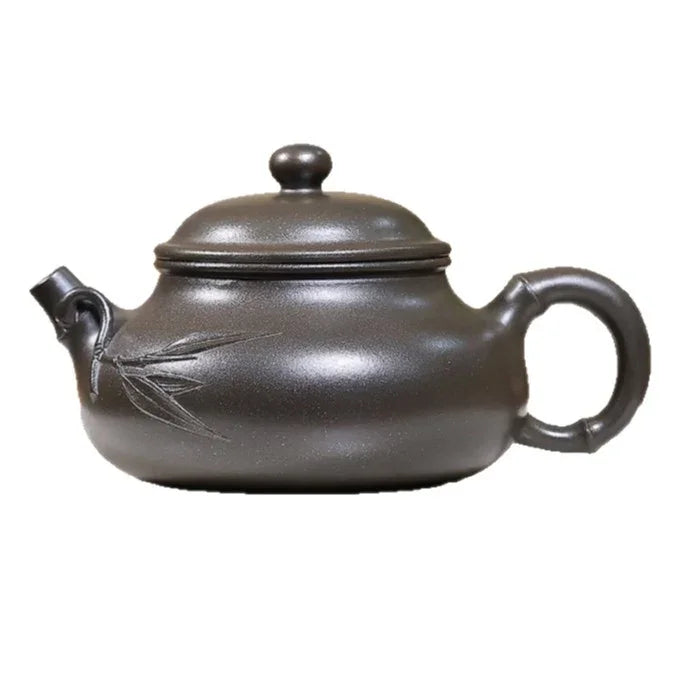 A dark brown ceramic teapot with a lid, bamboo leaf engraving on the side, and a curved handle, shown against a plain white background.