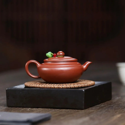 Red ceramic teapot with decorative elements on a dark surface