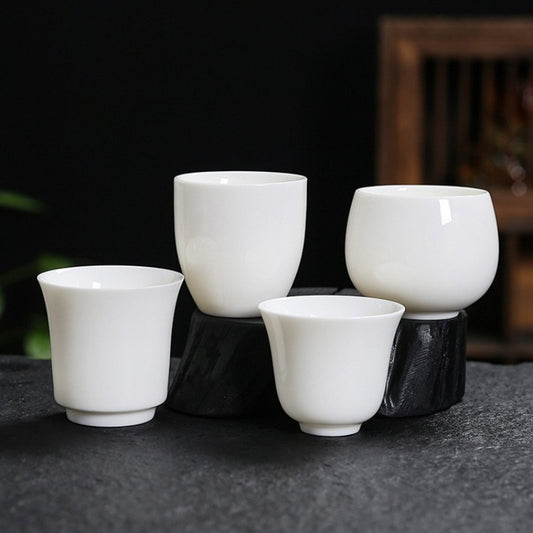 Four white ceramic tea cups of different sizes arranged on black stone risers against a dark background.

