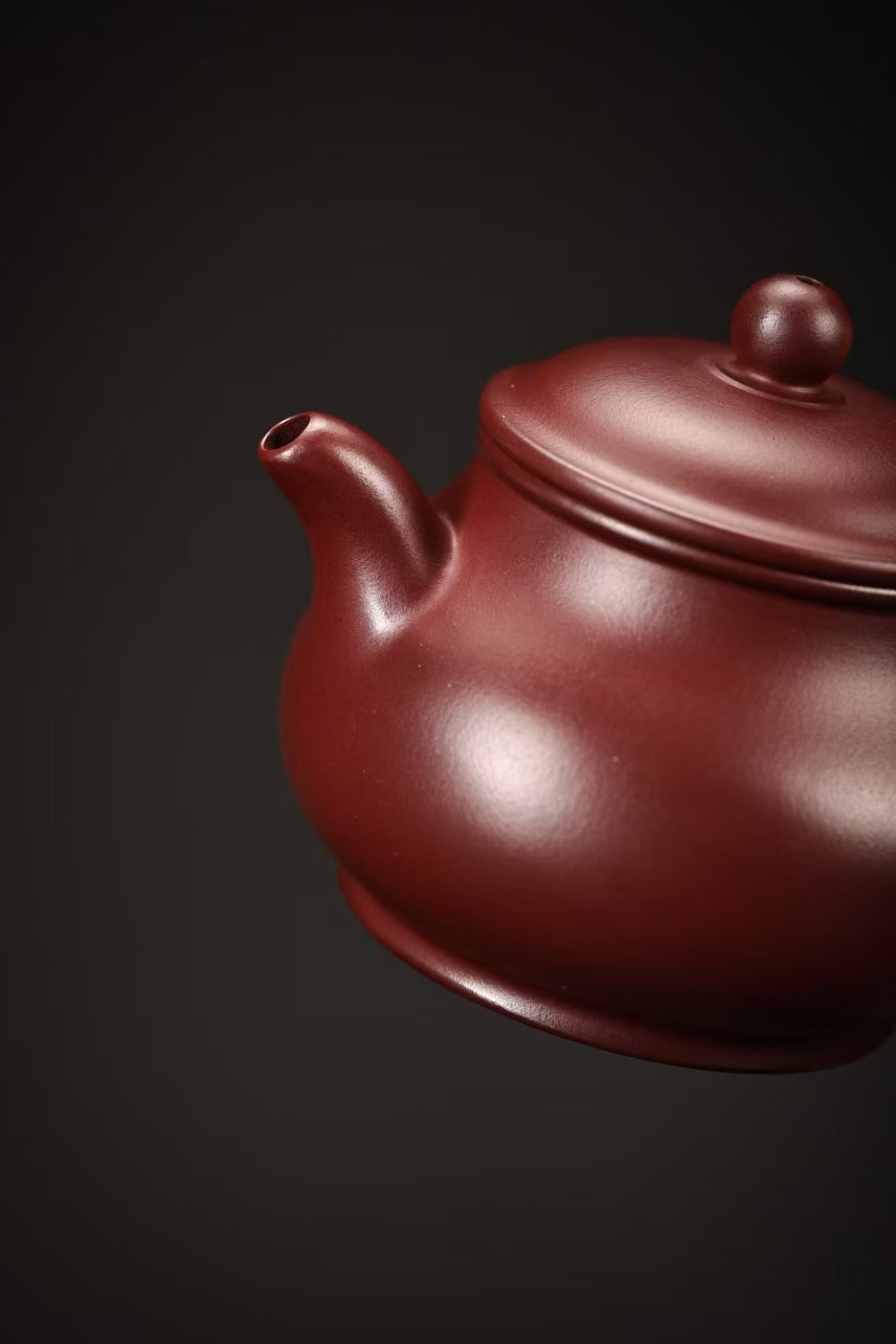 A close-up of a traditional Chinese Yixing clay teapot in a deep reddish-brown color, shown against a dark, solid background.

