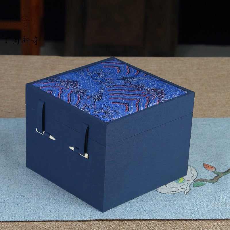 Three ornate cubic gift boxes with traditional East Asian-inspired designs on a wooden table