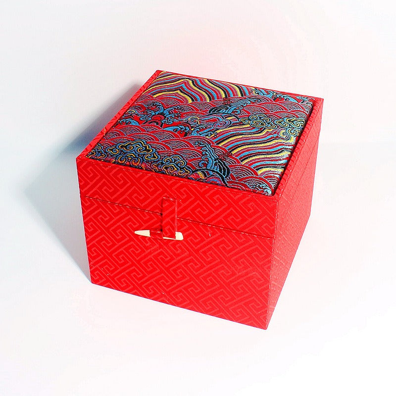 Three ornate cubic gift boxes with traditional East Asian-inspired designs on a wooden table