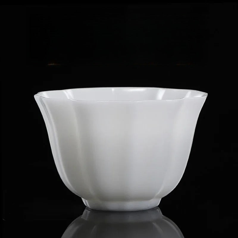 A white ceramic bowl with a flared rim and subtle vertical ridges, shown on a reflective black surface against a black background.

