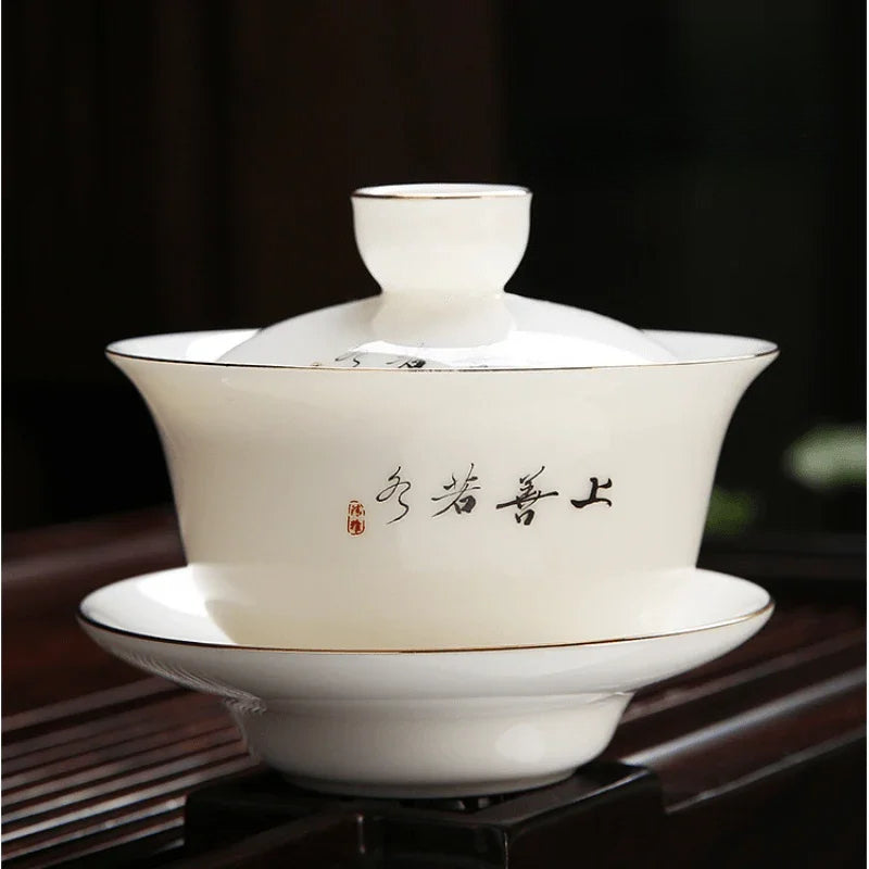 A white ceramic tea bowl set with a matching saucer, featuring gold trim and Chinese calligraphy on the side, displayed on a dark wooden surface.

