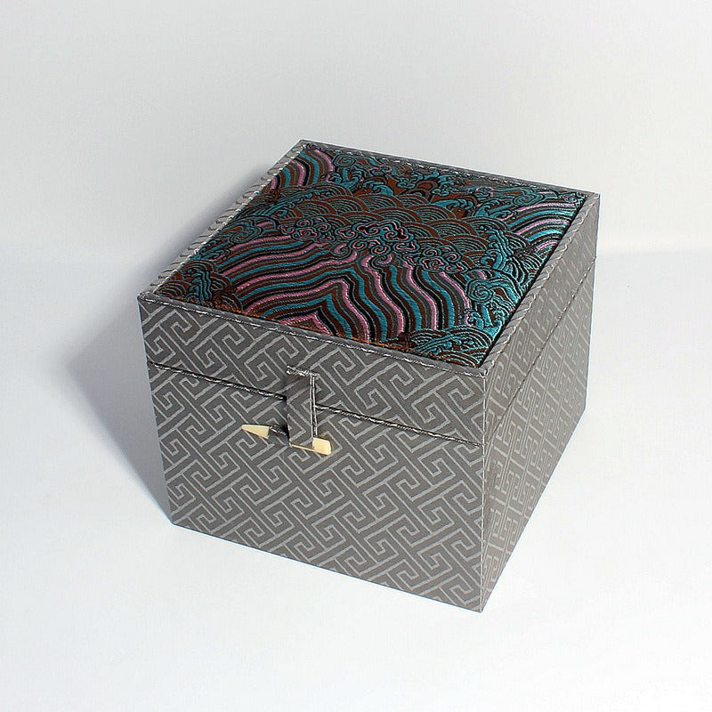 Three ornate cubic gift boxes with traditional East Asian-inspired designs on a wooden table