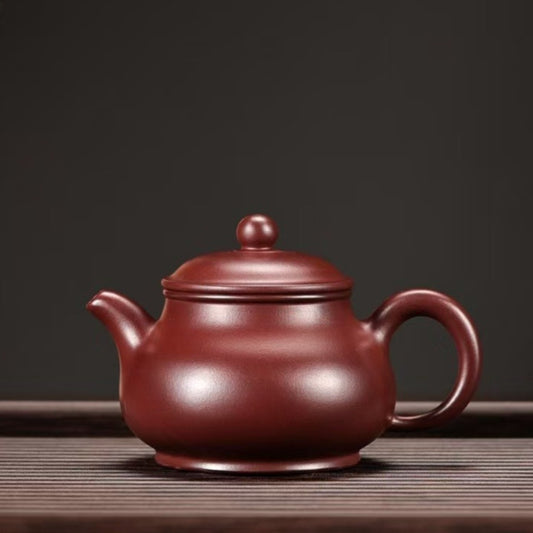 A classic Chinese Yixing Zisha teapot in a deep reddish-brown clay color, sitting on a dark wooden slatted surface against a dark gray background.

