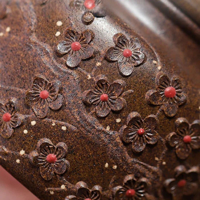 Close-up of a dark brown textured ceramic surface decorated with raised floral motifs and small red centers.

