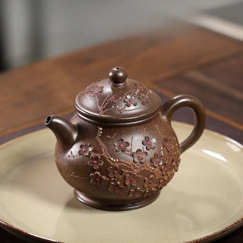 A brown ceramic teapot with raised floral details, resting on a beige plate over a wooden table.

