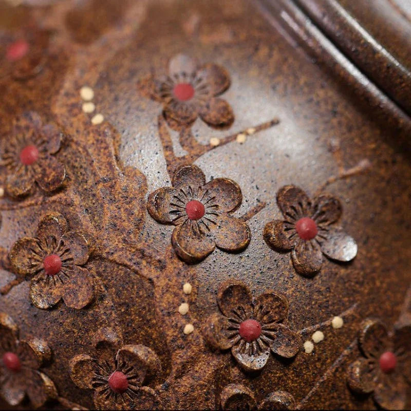 Close-up of a textured brown metal surface decorated with raised floral motifs and small red and cream accents.

