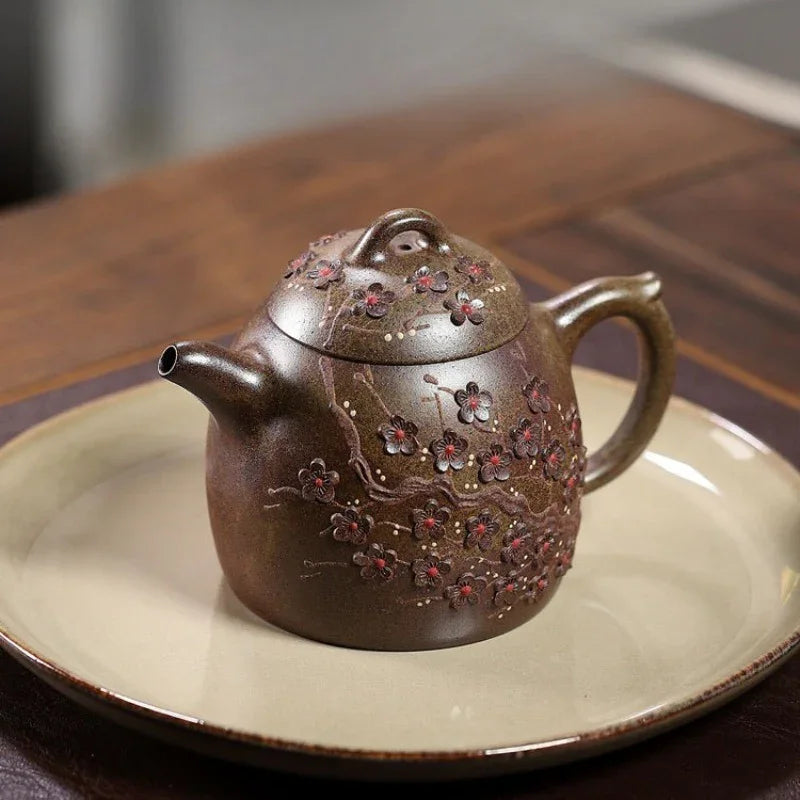 A brown ceramic teapot with floral relief decorations, resting on a beige ceramic plate over a dark wooden table.

