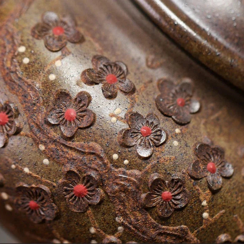 Close-up of a textured brown ceramic or pottery surface decorated with raised dark floral motifs and small red centers, with part of a rounded vessel edge visible at the top right.

