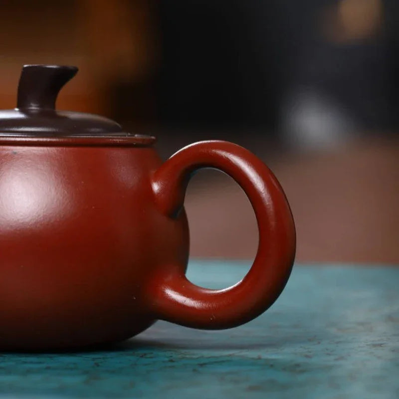 Red ceramic teapot on a textured surface with a blurred background

