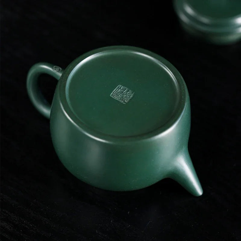 Green ceramic teapot with a logo on a dark background

