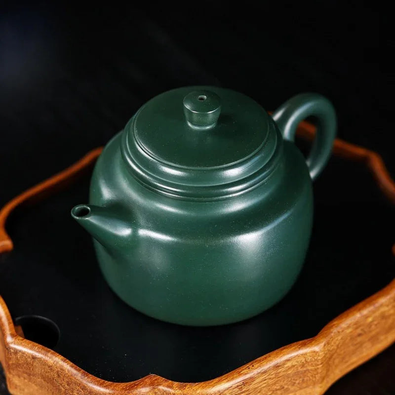 Green teapot on a wooden stand with a dark background

