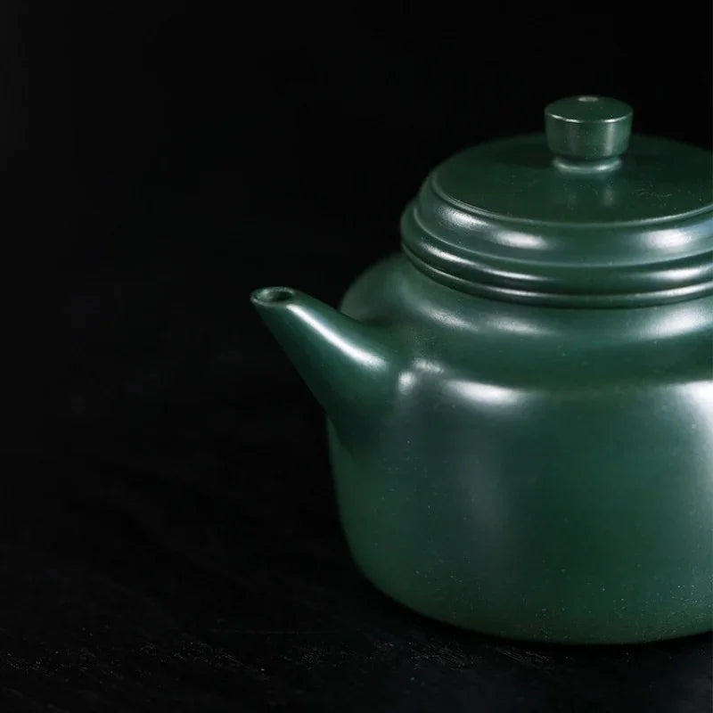 Green teapot on a black background

