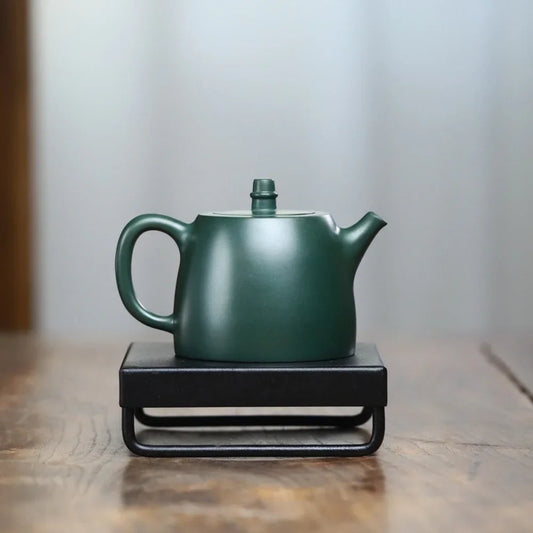 Green teapot on a black hot plate with a blurred background

