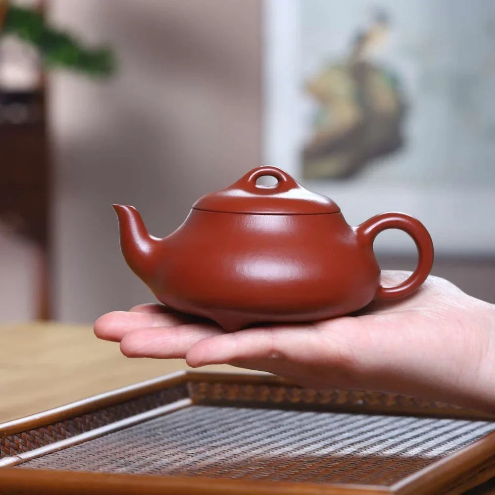 Red teapot held in a hand with a blurred background

