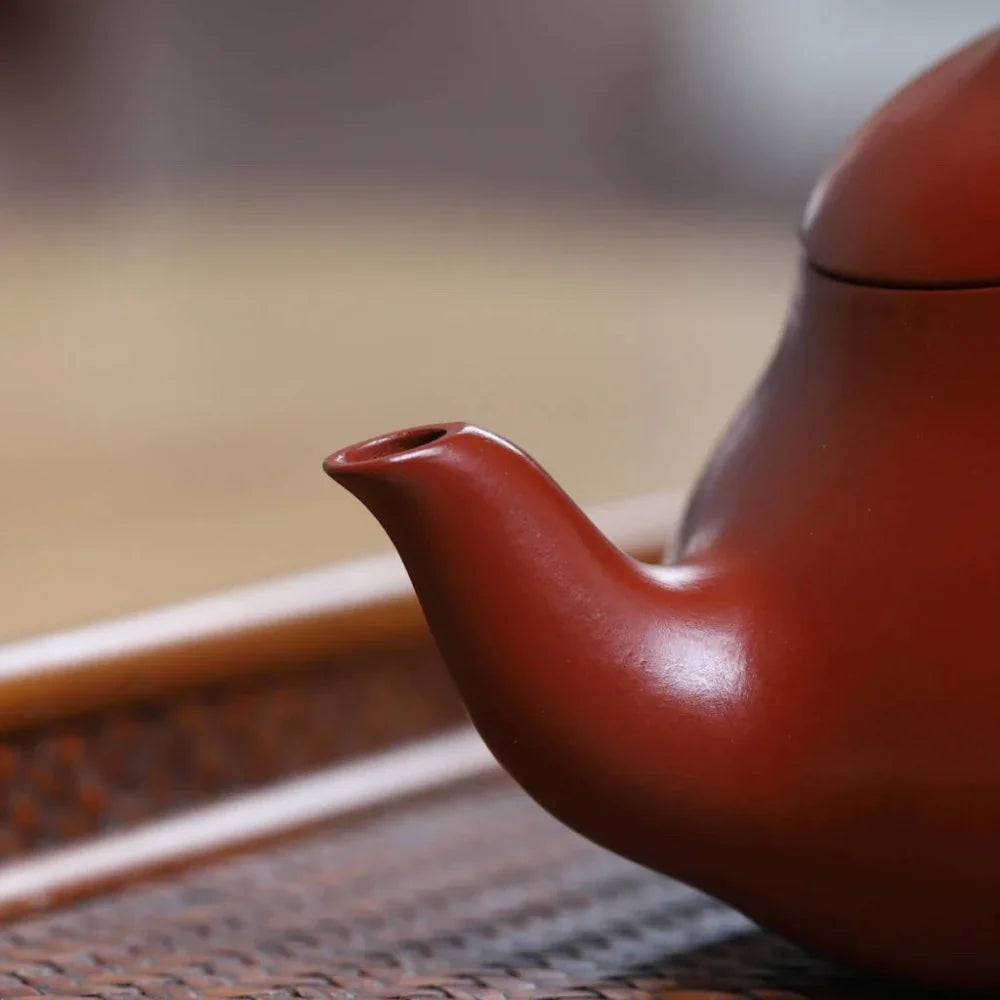 Red ceramic teapot on a woven surface with a blurred background

