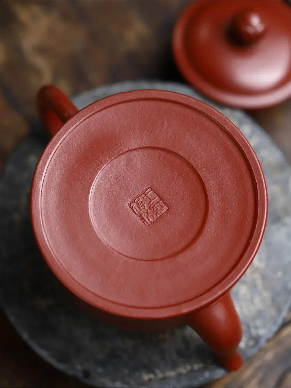 Red ceramic teapot with a visible brand logo on a textured surface

