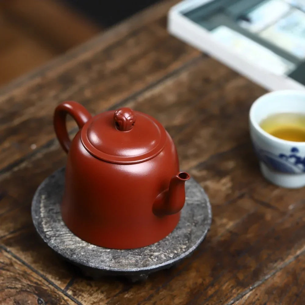 Red teapot on a wooden table with a cup of tea in the background

