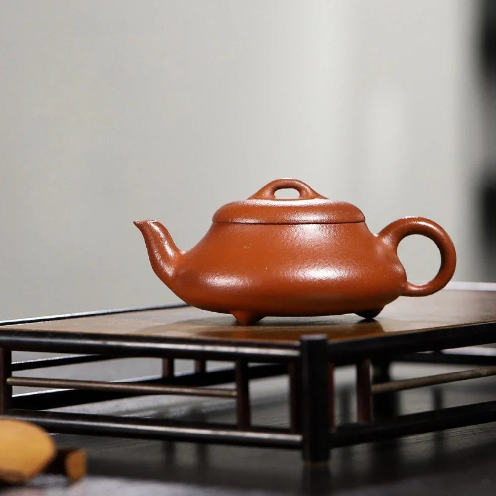 Red ceramic teapot on a wooden stand with a blurred background


