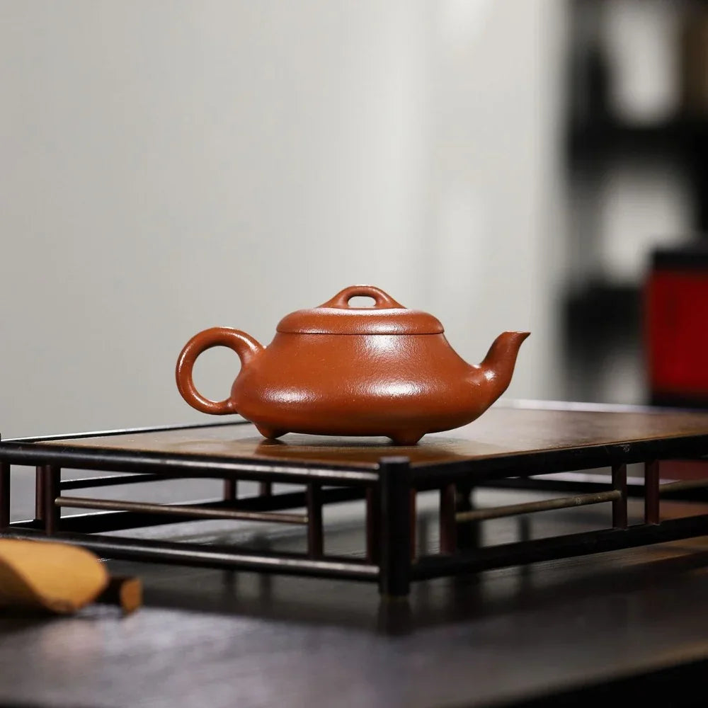 Red ceramic teapot on a wooden stand with a blurred background

