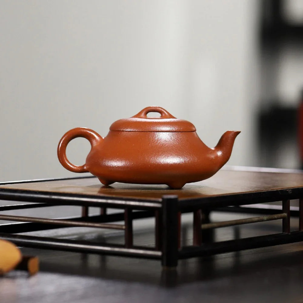 Red ceramic teapot on a wooden stand with a blurred background

