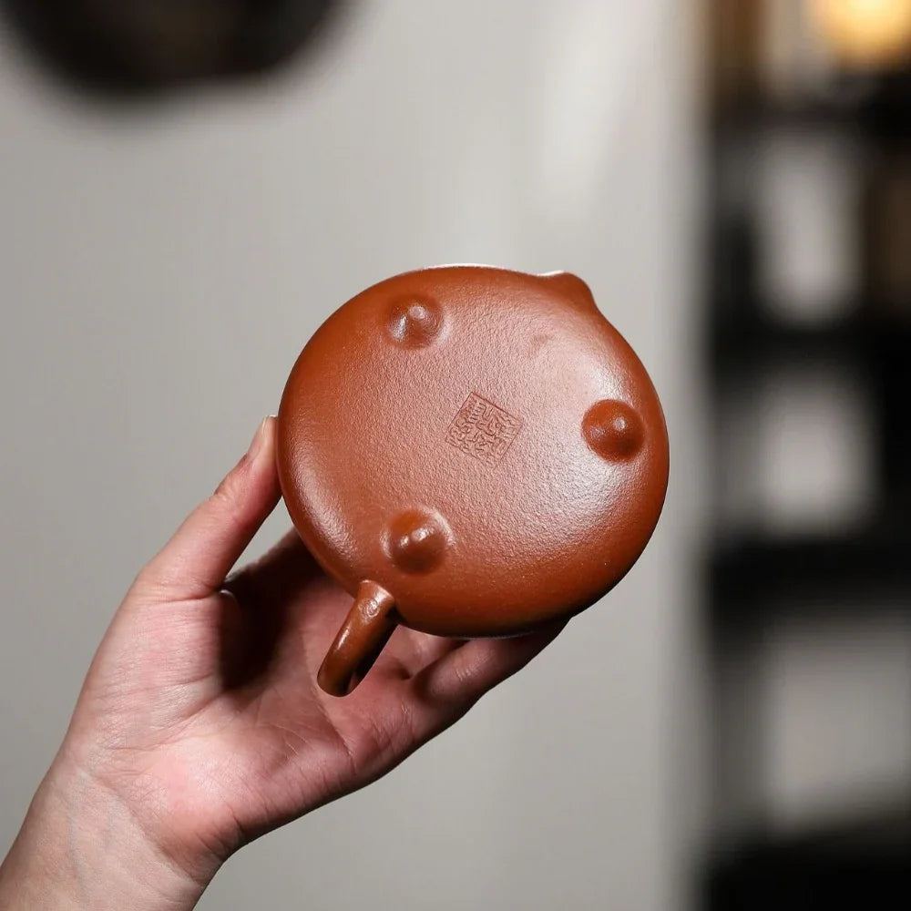 Hand holding a small brown ceramic pot with a blurred background

