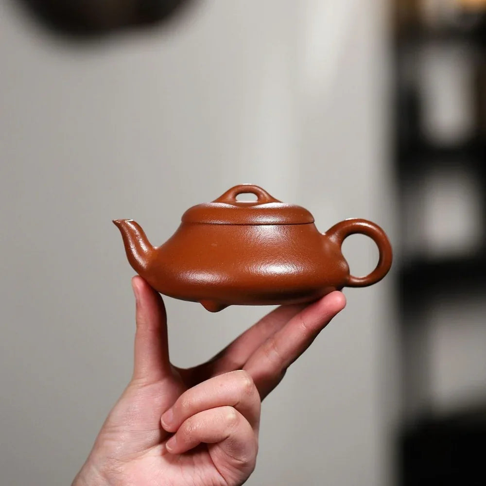Hand holding a small brown teapot against a blurred background

