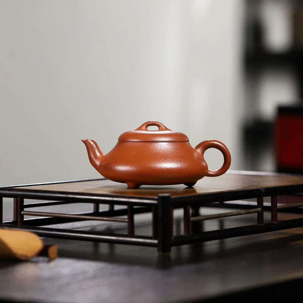 Red ceramic teapot on a wooden stand with a blurred background

