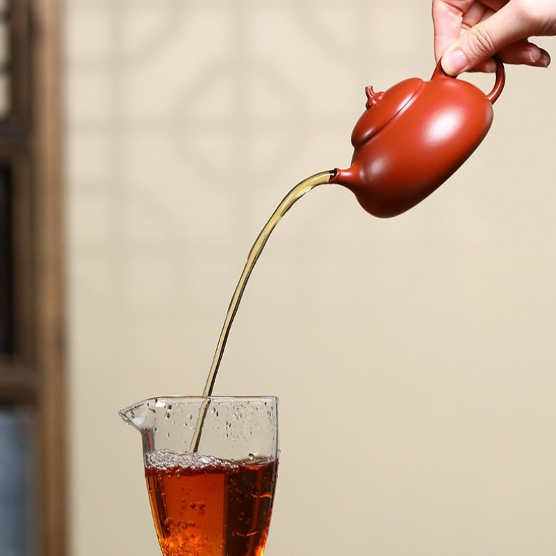 Red teapot pouring tea into a glass against a neutral background

