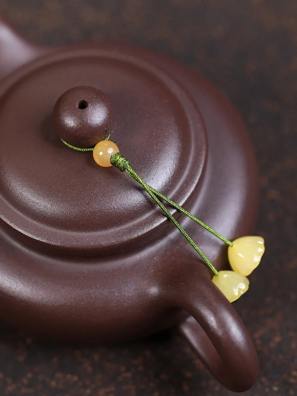 Close-up of a brown teapot lid with a string and yellow beads on a dark background


