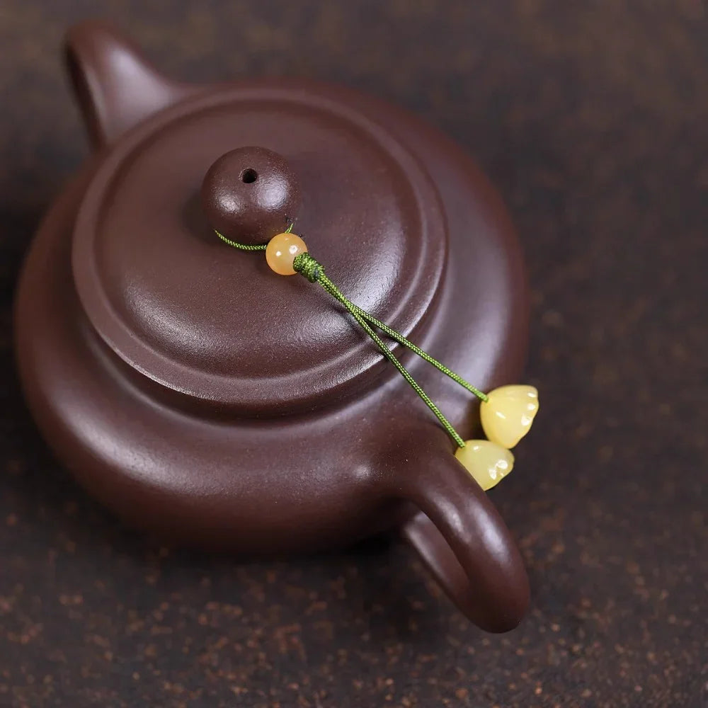 Brown ceramic teapot with decorative string beads on a dark background

