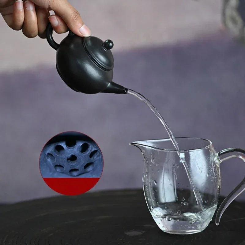 A hand holds a small black teapot pouring clear water into a transparent glass pitcher. A circular inset shows a close-up of the teapot's porous filter surface, with a red overlay at the bottom.

